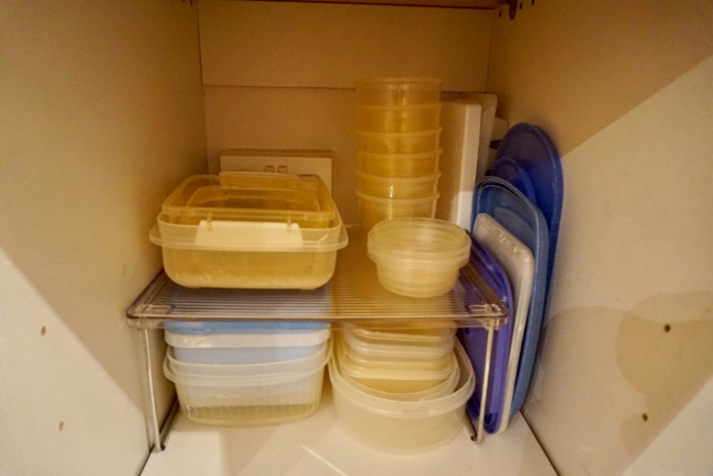 Tupperware being put back into the cupboard using the new cabinet shelf