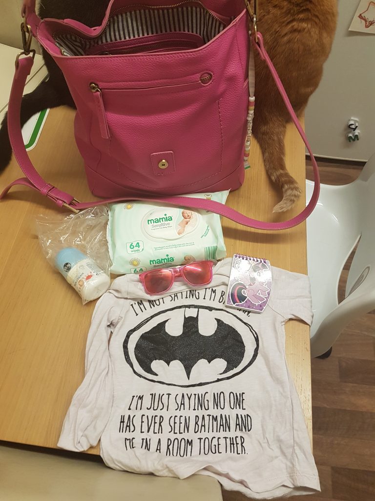 Pink handbag with content on table including a batman t-shirt and a pack of wipes